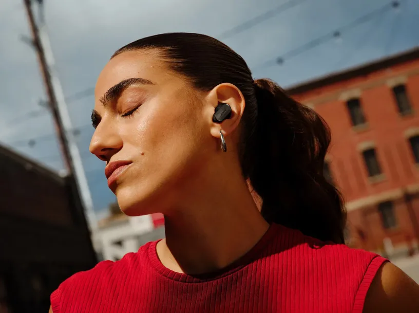 Woman wearing Bose QC Ultra Earbuds outdoors with eyes closed enjoying music